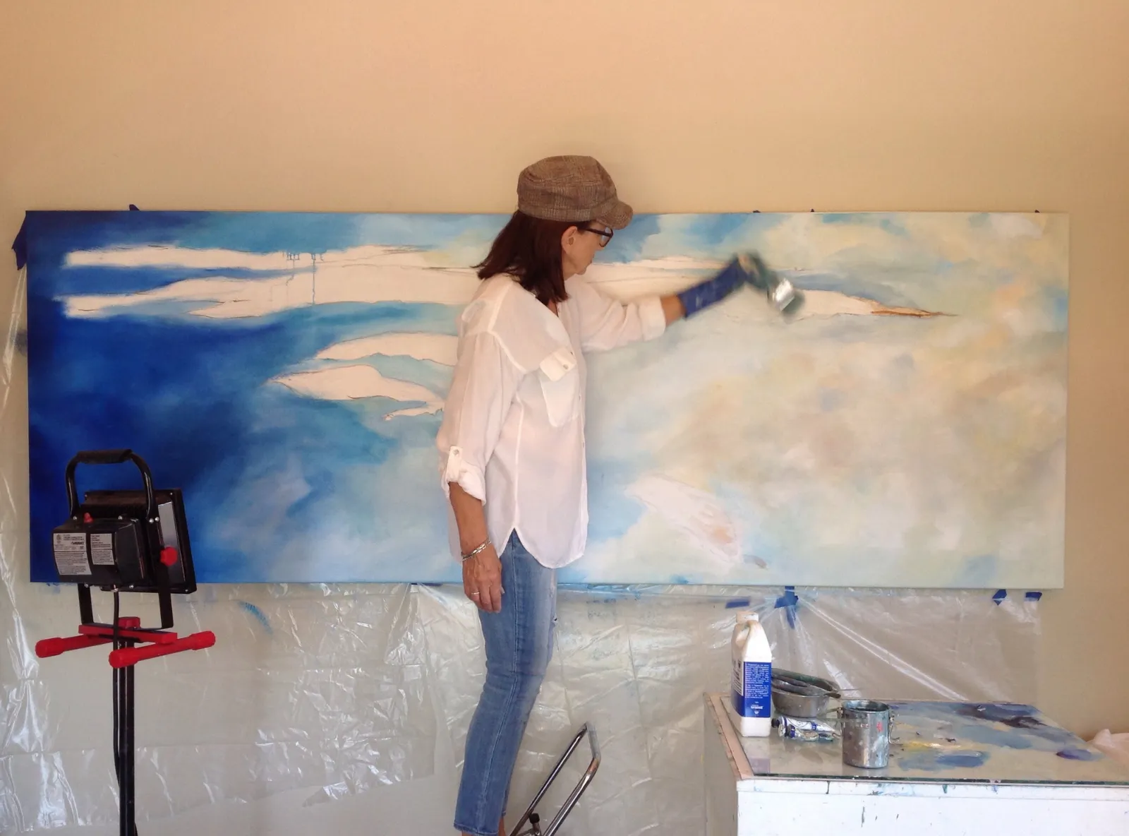 Michele Zuzalek in her studio painting a large blue-sky canvas
