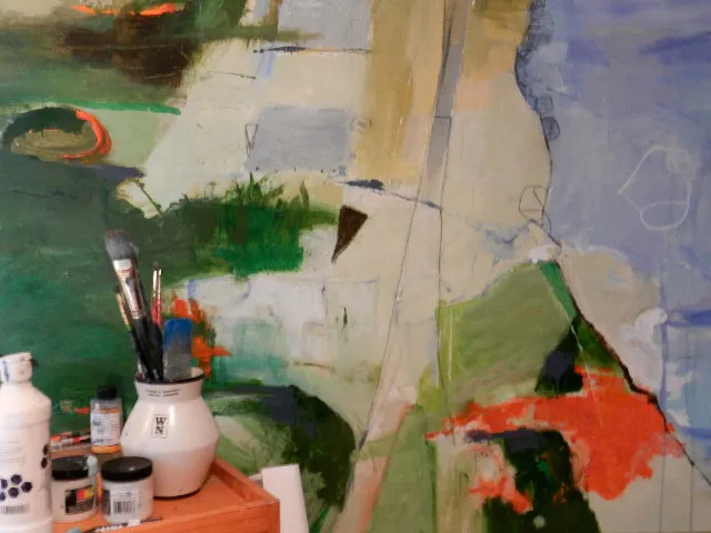 Close-up of a work in progress with brushes and paint jars in front of the canvas